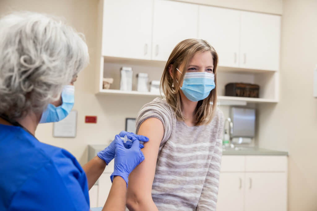 Woman is receiving a Covid-19 vaccination in doctor's office from senior nurse or doctor